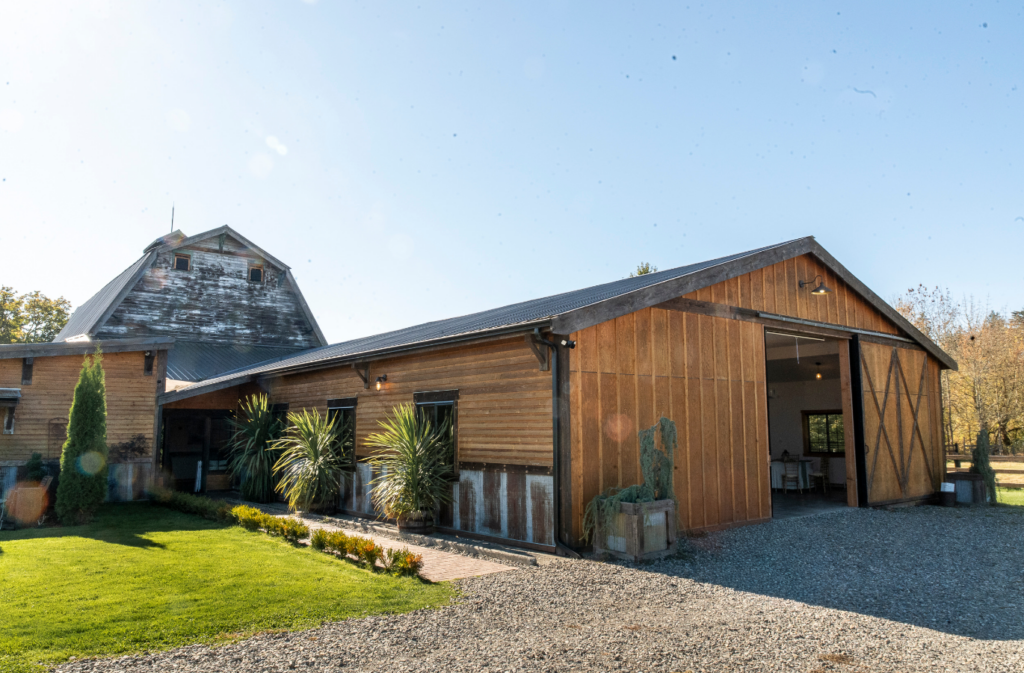 Rustic wooden barn with a large open doorway, a gravel driveway, and a manicured lawn.