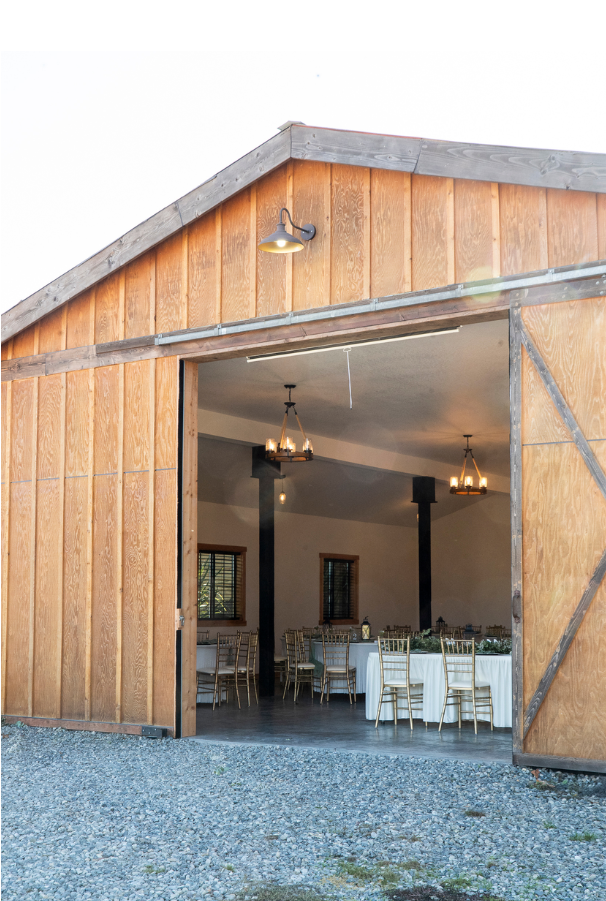Open wooden barn doors revealing a reception hall set with round tables and chairs.